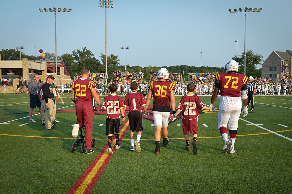 Football players walk onto the field with kids from Camp Good Days during a past Courage Bowl game.