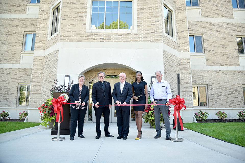 Matha Thornton, Fr. Mannara, President Rooney, Zahedie Martir, and Jack DePeters cut a ceremonial ribbon to mark the opening of Upper Quad Residence Hall.