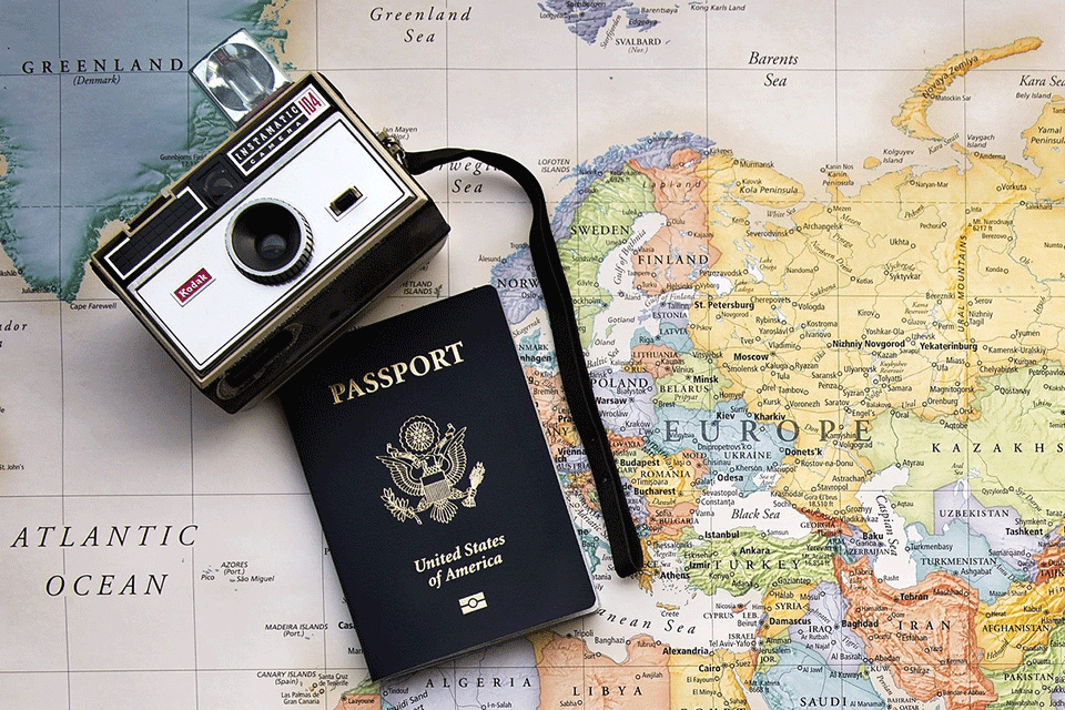 A passport and camera sit on top of a world map.