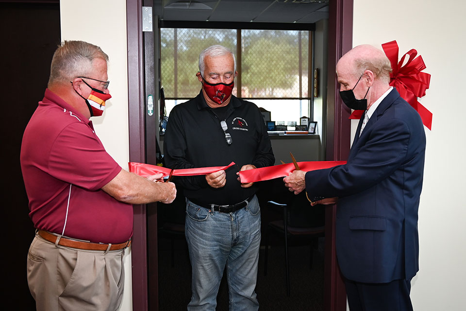 Mike Henchen, Terry Rodenbeck, and President Rooney cut the ceremonial ribbon on the newly named Cross Country Coach's Office