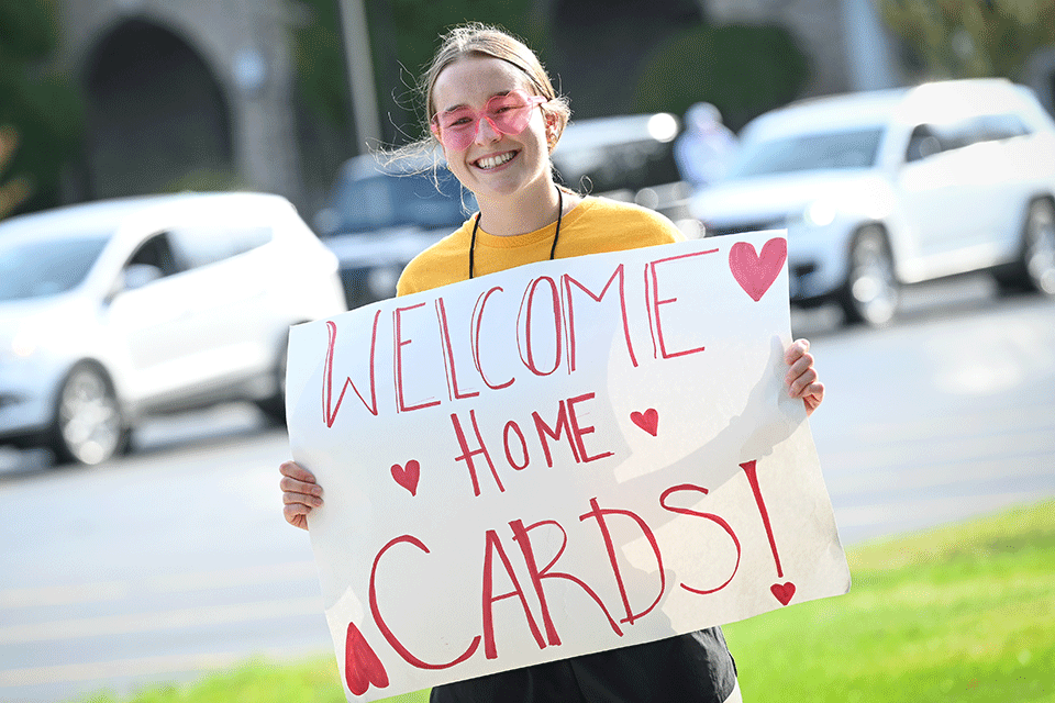 A student holds a sign that reads welcome home cards!