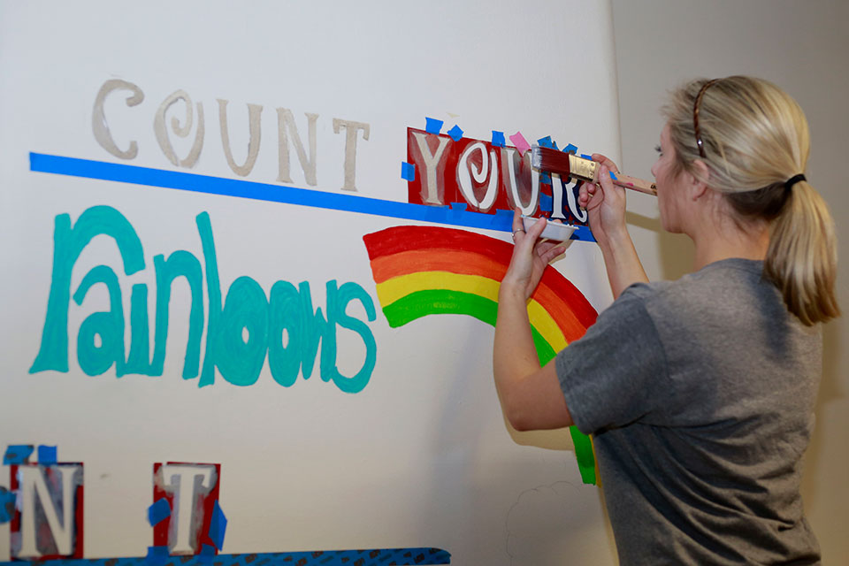 A student paints an inspiration quote on the wall of a local school during Color the Roc 2019.