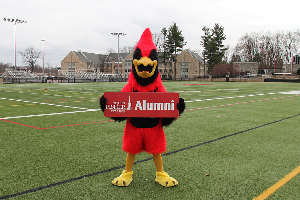 The Cardinal holds a sign welcoming alumni to campus.