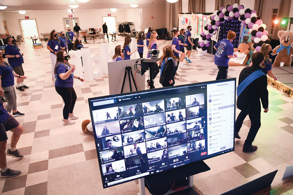 A computer screen with a Zoom meeting in the foreground and students dancing distanced in the background