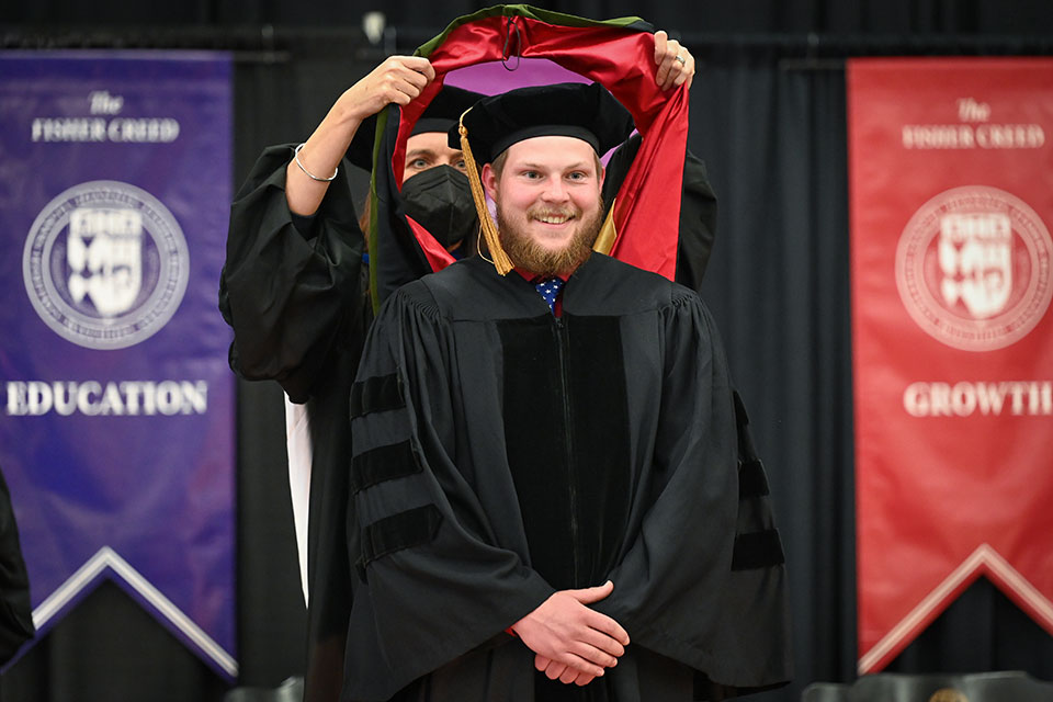 A graduate receives his doctoral hood from Dean Christine Birnie.