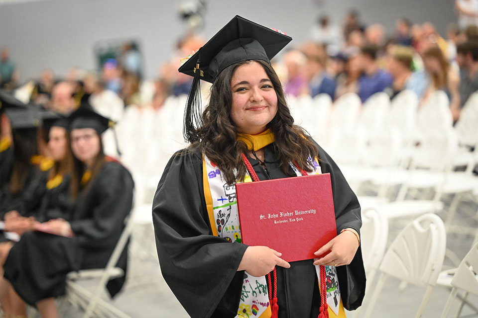 A graduate of the School of Education proudly holds up a diploma.