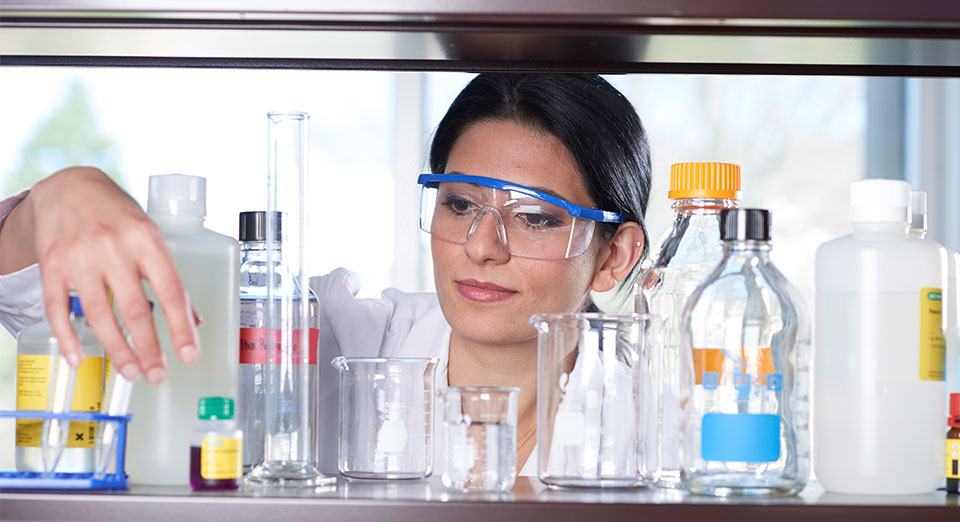 Female student behind beakers and pharmacy equipment.