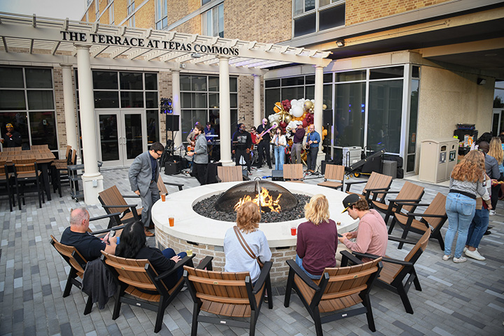 Students sit around a firepit at the Terrace at Tepas Commons while listening to live music.