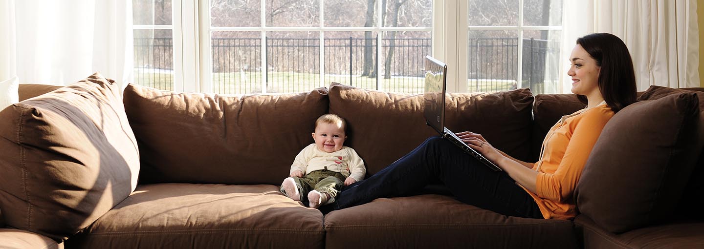 Student on couch with laptop and baby