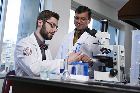 Pharmacy professor watches over male students in a lab setting.