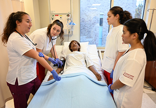 Four student nurses in simulated hospital setting caring for patient.