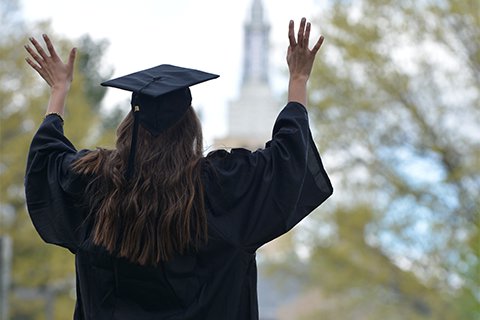 Student in cap and gown with arms raised.
